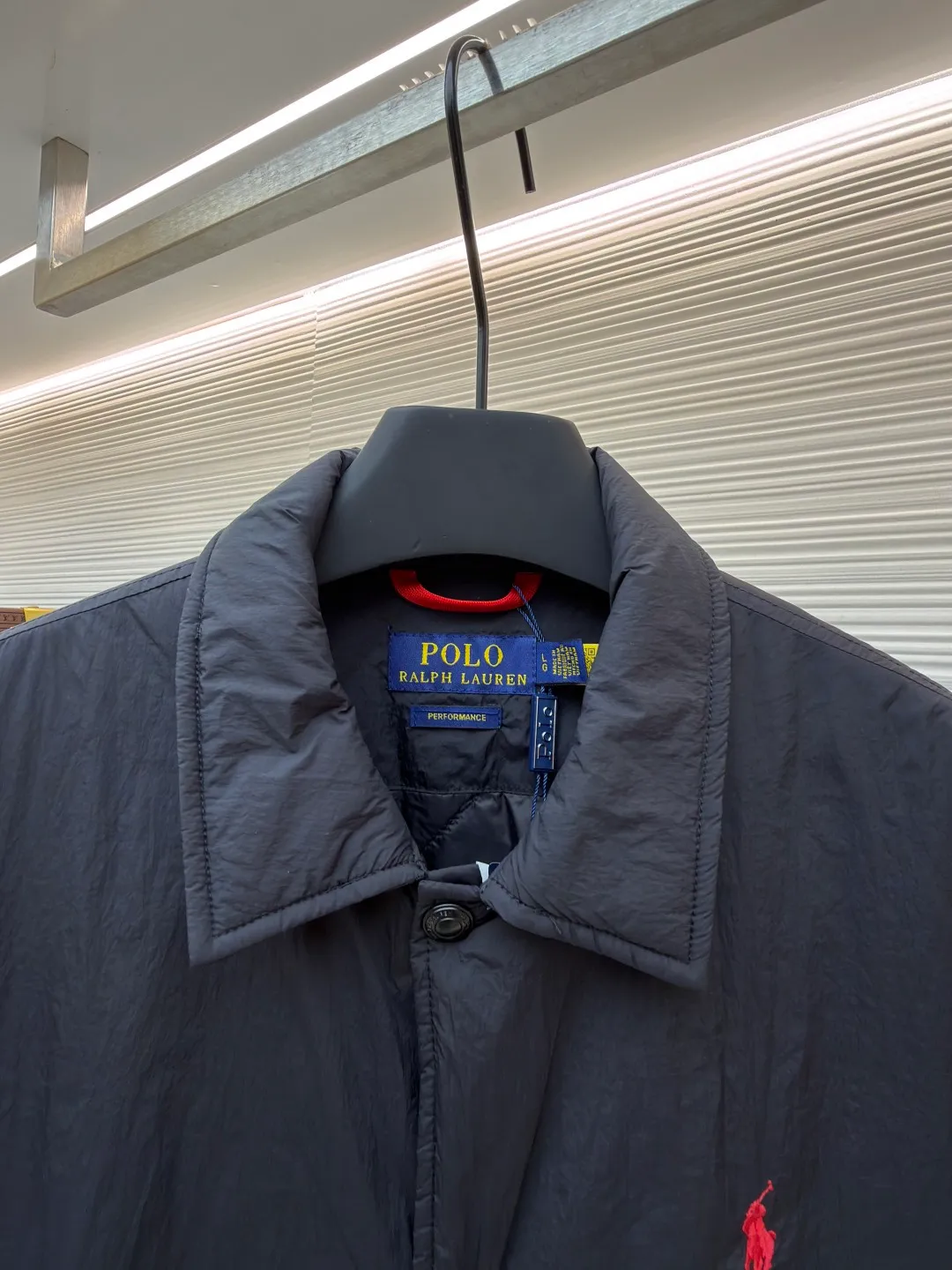 Ralph Lauren red label light cotton jacket (coach jacket) ●Original version: purchased and developed for 2699 ●Item number: 1681910-B90 ●Fabric: high-density nylon taffeta fabric ●Technology: embroidery production ●Color: black ●Version: fitted version ●Weight: about 340 grams ●Size: S-M-L-XL ●Description: The density of high-density nylon taffeta is about 210T-300T, with a smooth and slightly matte surface, excellent windproof and waterproof properties (with DWR water-repellent treatment), strong wrinkle resistance and easy care, in line with the positioning of American casual "durable and practical". Classic dark black, using vat dyeing process (dye penetrates into the fiber), the color fastness reaches ISO level 4 or above, preventing fading or color transfer after washing. The lightweight cotton-polyester blend lining (65% Polyester + 35% Cotton) reduces the friction between the fabric and inner clothing, improving the smoothness of wearing; the blended material combines breathability and durability to avoid the stuffy feeling of pure nylon lining. The classic Coach Jacket has a loose fit with slightly dropped shoulder lines (shoulder width is 1-2cm wider than the standard fit). The length reaches the hips and the sleeves are slightly tapered straight sleeves, taking into account both freedom of movement and casual style. Polo horse logo on the left chest: flat satin stitch embroidery (satin embroidery), embroidery thread: 100% polyester high color fastness embroidery thread (the color number is consistent with the brand's standard red color card), stitch density 12-15 stitches/cm, the outline of the horse logo is clear, and the details of the rider and horse are burr-free. Embroidery positioning: precise positioning through the template (12cm from the neckline and 8cm from the placket) to ensure left and right symmetry and centering. Topstitching technology: The seams of the body are made of double-needle flat seams (needle pitch 3cm/10 needles), the stitches are smooth and straight, the stitching color is dark black (the same color as the fabric), and the stitch width is 0.5cm, which enhances firmness while forming simple decorative lines. The splicing of the front placket and the body: the placket is made of double-layer folding + flat seam splicing, with a thickness of about 0.3cm to ensure that the buttons are not easily deformed when fixed; the edges of the placket are cut with a hot knife to avoid burrs. The sleeves are spliced ​​to the body: the armholes are spliced ​​with round-head keyhole machine seams + flat seams. After splicing, the armholes have a natural curvature and no sense of tightness during movement; the height of the sleeves is about 8-10cm, which is in line with the loose characteristics of casual jackets. Main button: black urea resin button, matte surface treatment, buttonholes are hand-made keyholes (6 strands of cotton thread, keyhole density 8 stitches/mm), and the edges of the eyelets are smooth and without burrs. Collar buttons: The first button on the collar is a hidden button (diameter 12mm), which prevents the collar from opening and improves the neatness of wearing.